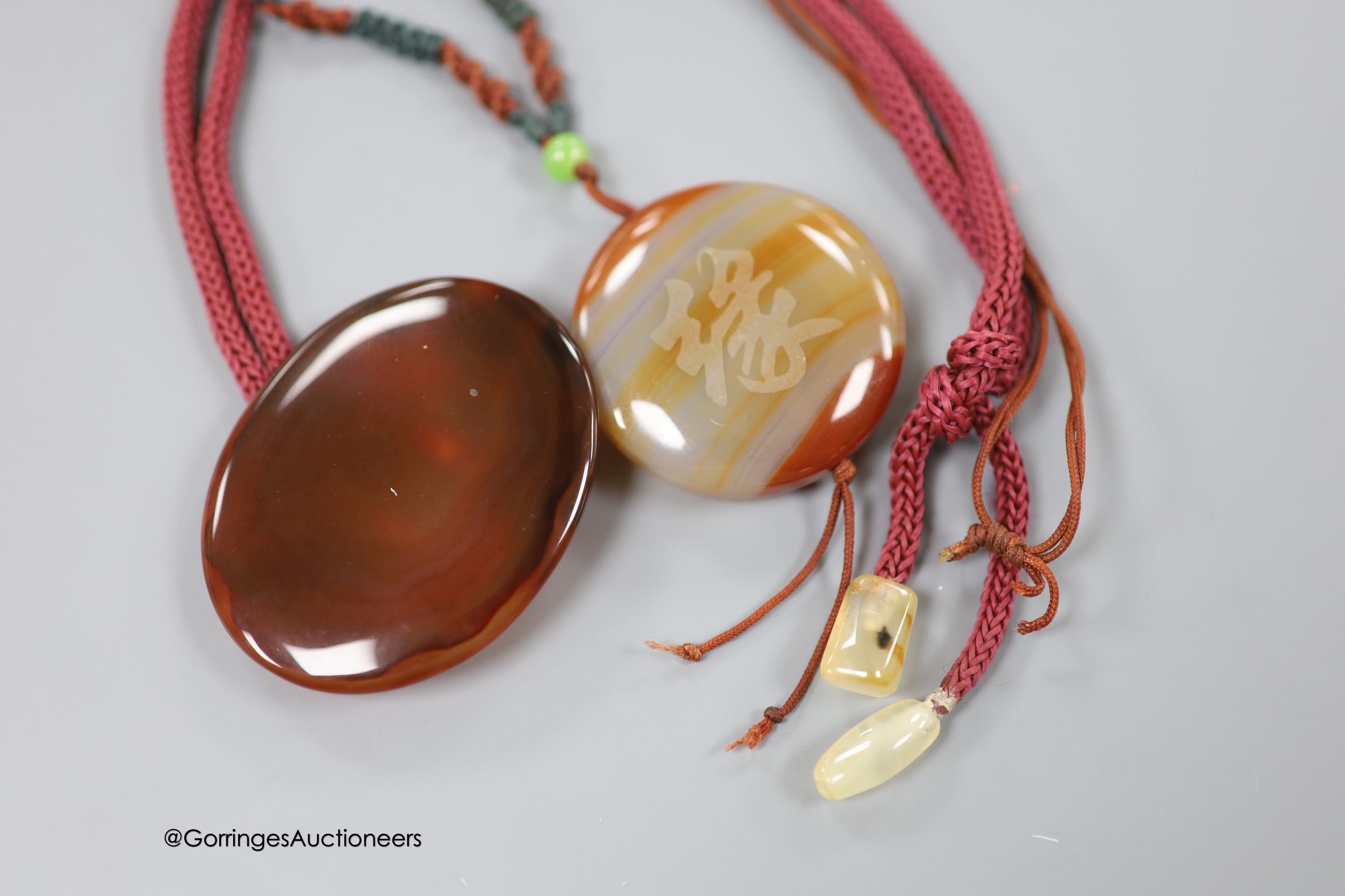 Two agate pendants, on fabric cords, largest pendant 57mm.